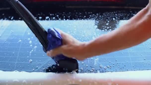穿着橙色衬衫的男人正在用蓝色布洗一辆白色的车 洗车用的是液体 — 图库视频影像
