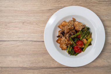 Teriyaki soslu kızarmış kırmızı levrek ve çeşitli sebzeler: brokoli, domates, kuşkonmaz ve ahşap masada bebek mısırı..