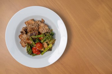 Teriyaki soslu kızarmış kırmızı levrek ve çeşitli sebzeler: brokoli, domates, kuşkonmaz ve ahşap masada bebek mısırı..