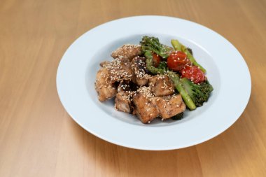 Teriyaki soslu kızarmış kırmızı levrek ve çeşitli sebzeler: brokoli, domates, kuşkonmaz ve ahşap masada bebek mısırı..