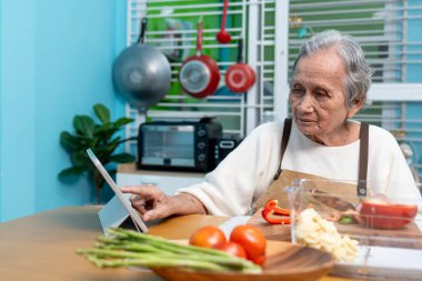 Yaşlılar mutfağında yemek pişiriyor ve yemek pişirmeyi öğrenmek için dijital tabletlere bakıyor..