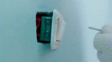 Yakından çekilen, kumaş eldiven giyen ve tornavidayı kullanarak tamir için bir ışık düğmesi paneli kullanan bir adam..