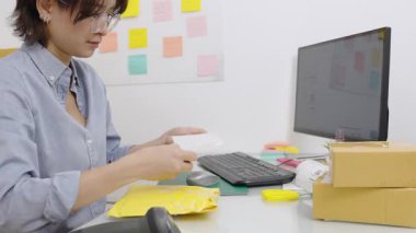 Asyalı kadın ofis çalışanı paket kutularını barkod etiketlerini okuyarak bilgisayardaki bilgileri kaydetmek için barkod tarayıcısıyla kontrol ediyor..