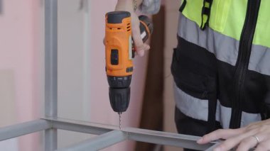 Yansıtıcı yelek giyen kadın işçiler çelik ya da alüminyum delmek için kablosuz çelik matkaplar kullanıyorlar..