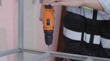 Yansıtıcı yelek giyen kadın işçiler çelik ya da alüminyum delmek için kablosuz çelik matkaplar kullanıyorlar..