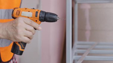 Yansıtıcı yelek giyen erkek işçiler çelik ya da alüminyum delmek için kablosuz çelik matkaplar kullanırlar..