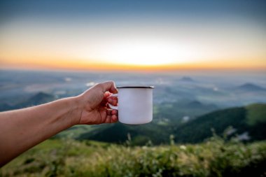 Gün batımının arkaplanına karşı dağlarda elinde fincanla