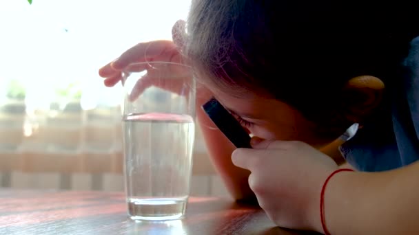 Dziecko patrzy na wodę szkłem powiększającym. Skupienie selektywne. — Wideo stockowe