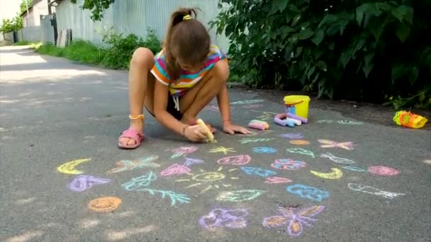 The child draws with chalk on the asphalt. Selective focus. — Stock Video