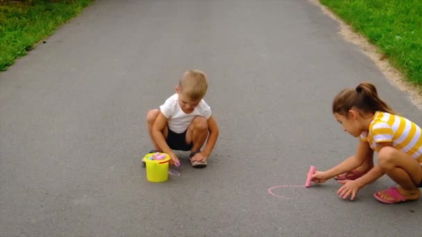 Barn tegner med kritt på asfalten. Selektivt fokus. – stockvideo
