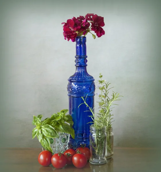 Blue glass bottle with vegetables and flowers — Stock Photo, Image