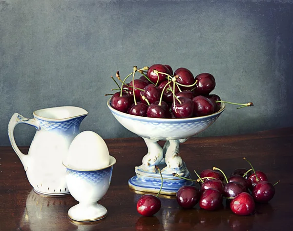 Still life, cherries, milk jug, cooked egg on a wooden table — Stock Photo, Image