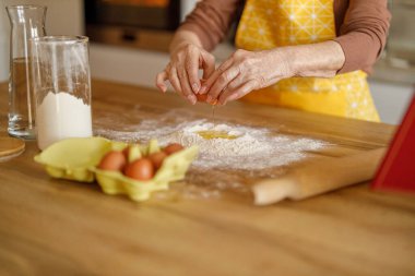 Blog 'una şeker hazırlarken mutfak tezgahında una yumurta kıran yaşlı kadının elleri.