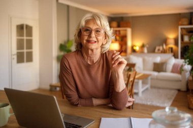 Not defteri ve dizüstü bilgisayarı olan kendinden emin yaşlı bir kadının portresi elinde kalem ve evde aylık bütçe planlaması tutuyordu.