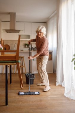 Parke mutfak zeminini kovayla paspaslarken şarkı söyleyen mutlu son sınıf öğrencisi kadın.