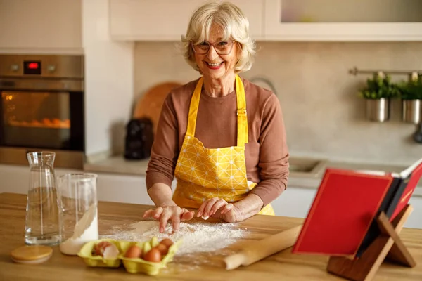 Adada un pişirirken yemek blogu için kurabiye hamuru yapan önlüklü yaşlı kadının portresi.
