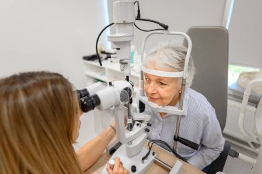 Modern klinikte doğru görüş kontrolü için yaşlı bir kadının gözlerini kesme lambasıyla inceleyen kadın göz uzmanının yüksek açılı görüntüsü