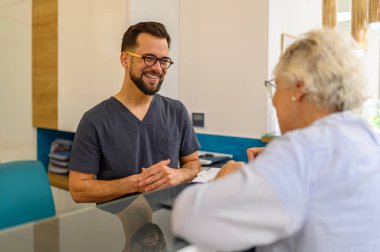 Hastane ziyareti sırasında resepsiyonda erkek doktorla sağlık sorunlarını tartışan yaşlı bir kadın.
