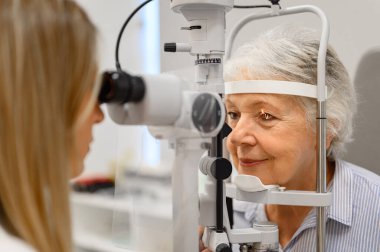 Görme kontrolü için göz hekimliği kliniği ziyareti sırasında son sınıf öğrencisini lambayla muayene eden kadın doktor.