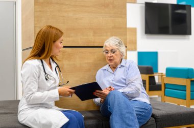 Kadın göz doktoru hastanede yan yana otururken yaşlı hastaya görme testi raporları gösteriyor.