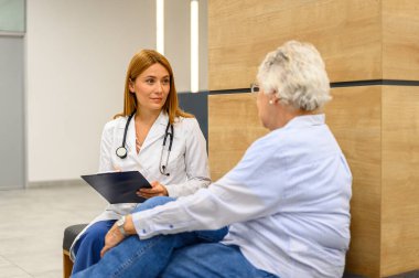 Hastane ziyareti sırasında yaşlı kadınla konuşurken panoya tıbbi gözlemler yazan kadın doktor.