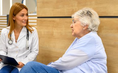 Hastane ziyareti sırasında hastanede oturan yaşlı hastaya teşhis raporunu açıklayan kendinden emin bir kadın doktor.