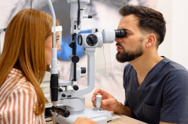 Erkek göz doktoru, klinikteki rutin vizyon kontrolü sırasında kadın hastaların gözlerini incelemek için kesik lamba kullanıyor.