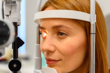 Göz muayenesi sırasında göz bebeğine kesik lamba tutulan genç bir kadının yakın çekimi.