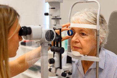 Kesik lamba testi sırasında yaşlı bir kadının klinikteki gözlerini incelemek için teşhis merceği kullanan kadın göz doktoru.