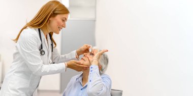 Kadın doktor, rutin vizyon tedavisi için göz doktoru muayenesi sırasında yaşlı hastanın gözüne göz damlası koydu.