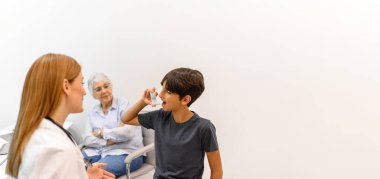 Kıdemli kadın torununa bakıyor. Rutin pediatri kliniği ziyareti sırasında kadın doktorla birlikte astım pompasından nefes alıyor.