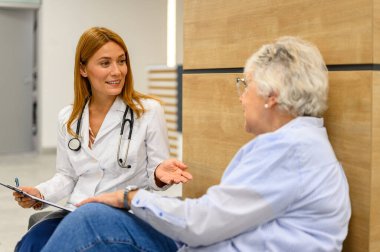 Kendine güvenen kadın göz doktoru, rutin kontroller sırasında hastanede oturan kıdemli bir hastayla görme testi sonuçlarını tartışıyor.