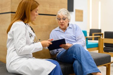 Laboratuvar önlüklü kadın doktor, hastanede test sonuçlarını tartışırken kıdemli hastaya tıbbi raporları gösteriyor.