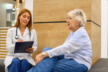 Hastanede oturan yaşlı bir hastayla konuşurken teşhis ayrıntıları yazan kadın göz doktoru.