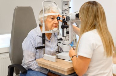 Modern oftalmoloji kliniğinde yaşlı kadının gözlerini kesik lamba lensleriyle inceleyen kadın göz doktoru.