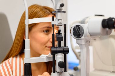 Optalmoloji kliniğinde rutin göz muayenesi sırasında kadın hastanın göz bebeğini aydınlatan kesikli lambanın yakın çekimi.