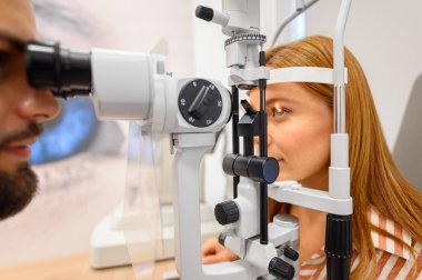 Modern klinikteki rutin kontroller sırasında erkek göz doktoru kadın hastaya kesik lamba göz değerlendirmesi yapıyor.