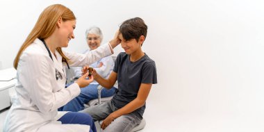 Büyükannem, erkek çocuğa reçeteli ilaç veren kadın çocuk doktoruna bakıyor. Hastanede saçlarına hafifçe dokunarak onu rahatlatıyor.