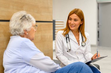 Hastanede oturan yaşlı bir hastayla konuşurken teşhis ayrıntıları yazan kadın göz doktoru.