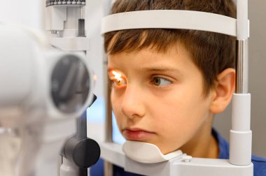 Optalmoloji kliniğinde vizyon kontrolü için kesik lambayla göz muayenesi yapılan sevimli bir çocuğun yakın çekimi.