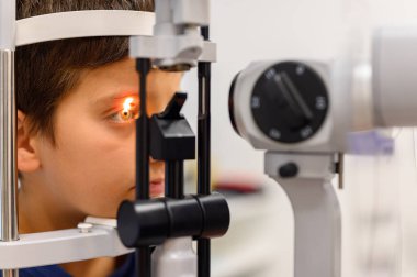 Göz muayenesi sırasında göz bebeğine kesik lamba ışığı tutarak göz muayenesi yapılan çocuğun yakın çekimi.