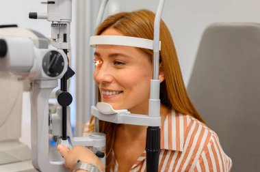 Close-up of young woman undergoing eye test with slit lamp light directed at eyeball during checkup at clinic