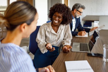 Masasında dizüstü bilgisayarı ve not defteri olan neşeli bayan avukatlar tartışırken, iş adamları modern ofisin arka planında raporlar hazırlıyorlar.
