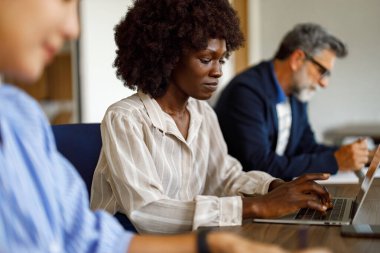 Modern ofis çalışma alanındaki iş arkadaşlarıyla iş birliği yaparken dizüstü bilgisayardaki odaklı muhasebeci raporunu analiz ediyor