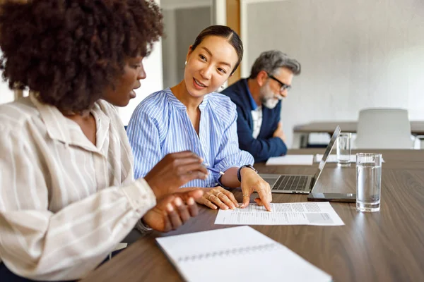 Ofisteki arka planda iş adamıyla finansal belgeleri analiz eden ve tartışan kadın meslektaşlar.