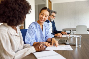 Modern ofisin arka planında erkek iş arkadaşıyla finans raporunu tartışan kadın profesyoneller.