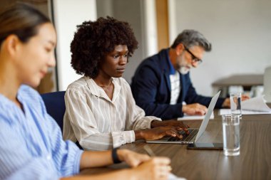 Modern ofisteki iş arkadaşlarıyla çalışırken dizüstü bilgisayara odaklanan ve verileri analiz eden iş kadını.