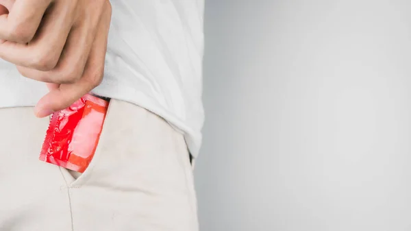 Man wearing white t-shirt and hand pulled red condom out of the pant pocket. Concept of Safe sex. Reduce of pregnancy and sexually transmitted disease.