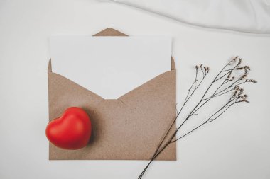 Açık kahverengi kağıda kırmızı kalp ve limonyum kuru çiçek ve beyaz arka planda beyaz bez konur. Sevgililer Günü konsepti