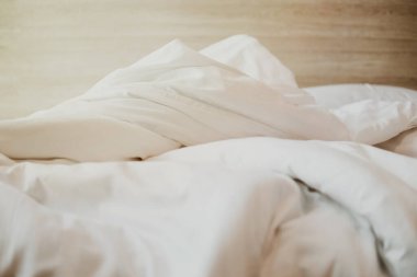 Beyaz yataklı yatak odası, beyaz yorgan, tahtadan yatak başlığı ve güneş ışığı olan yatak odası.